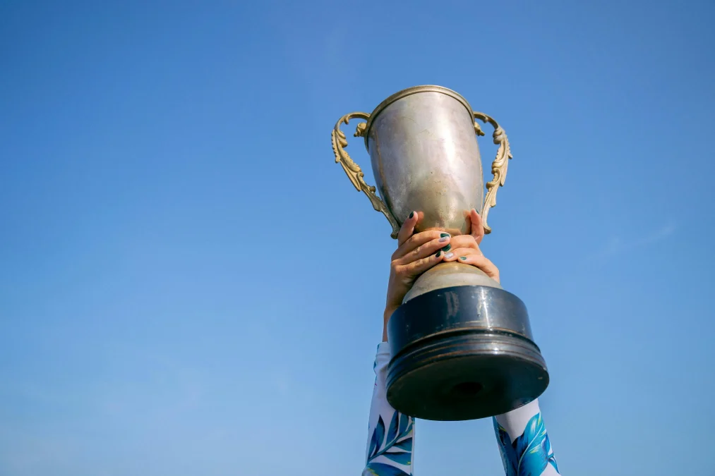 Hands holding a trophy high against a clear blue sky symbolizing victory in community contests
